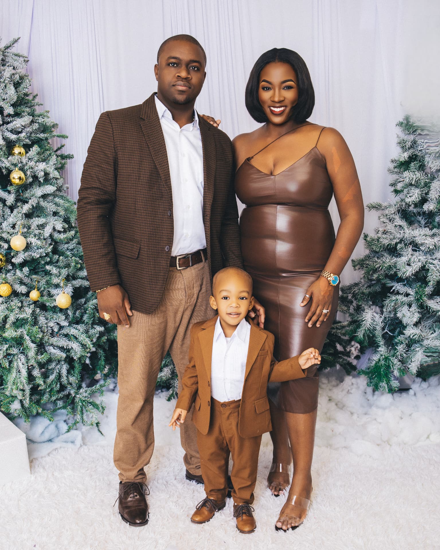 Family of three standing together between snow-dusted Christmas trees