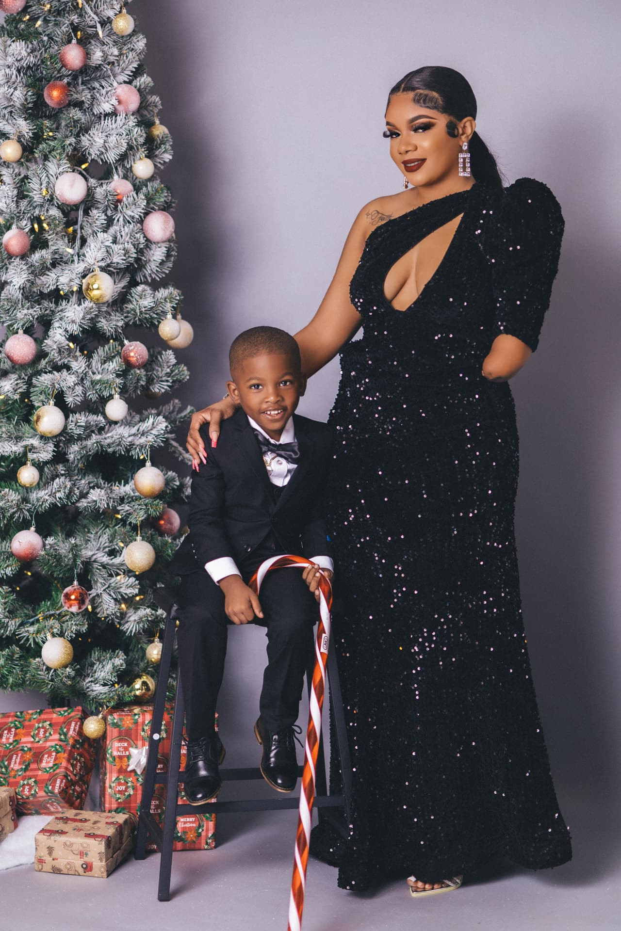 Young son holding an oversized candy cane prop beside a frosted Christmas tree