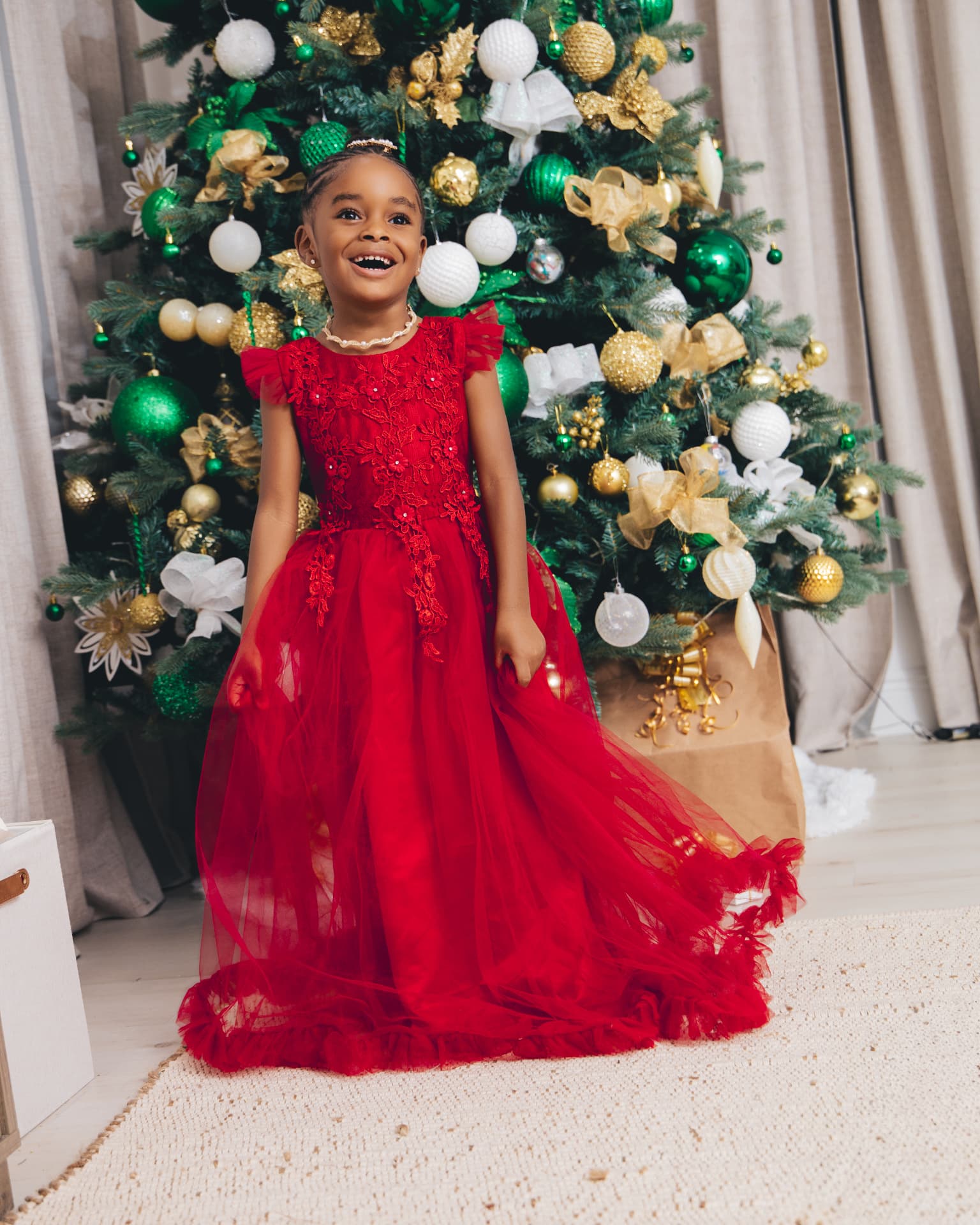 Young girl in a red tulle gown laughing beside a Christmas tree decorated in green, white and gold